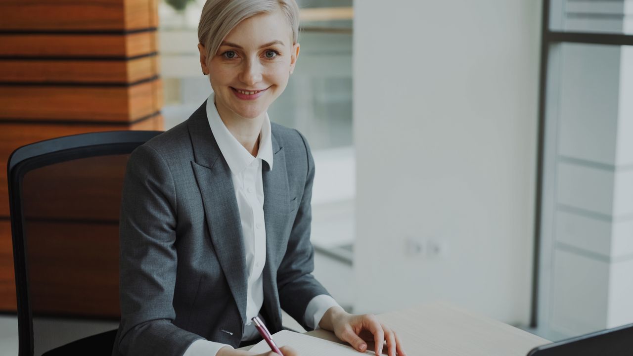 Hello world! Professional businesswoman smiling at desk in modern office environment.
